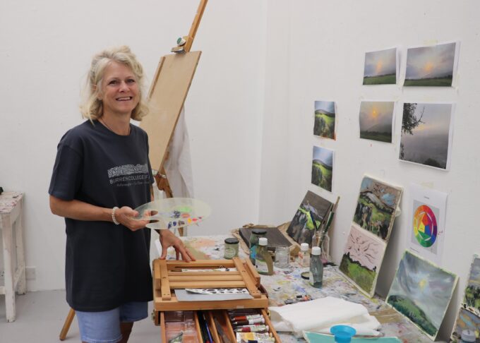 Workshop participant wearing Burren College of Art tshirt smiling in front of small paintings
